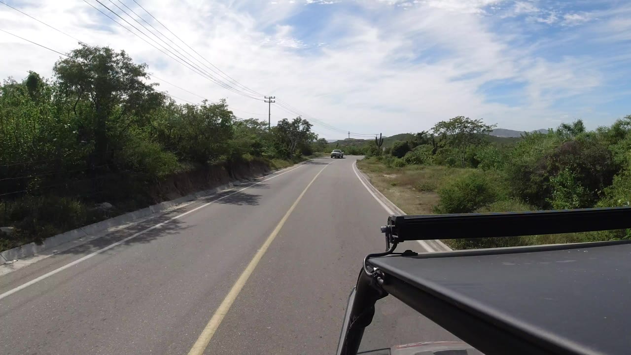 Two-lane road ahead with green roadside brush and vehicle hardware in the foreground.