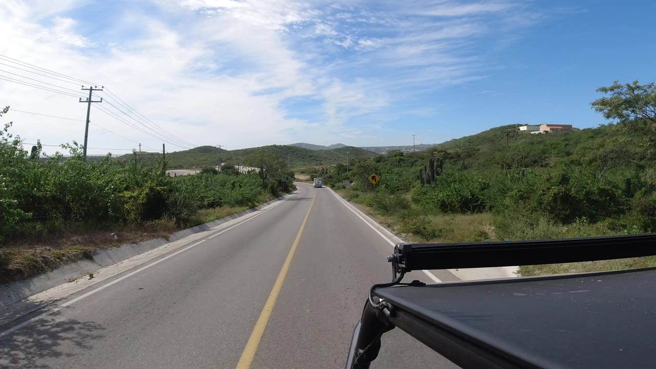 Sunny highway view with utility poles, brush, hills, and a distant vehicle.