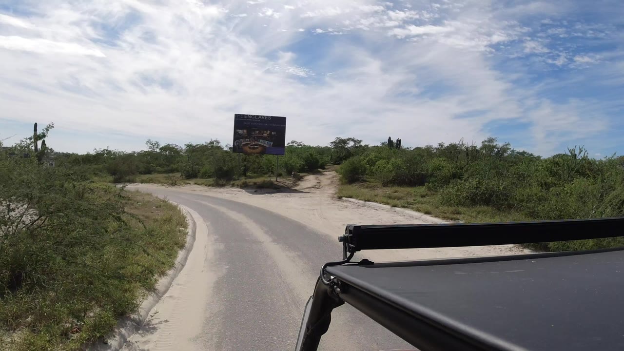 Curving paved road with scrub vegetation and a roadside sign ahead.