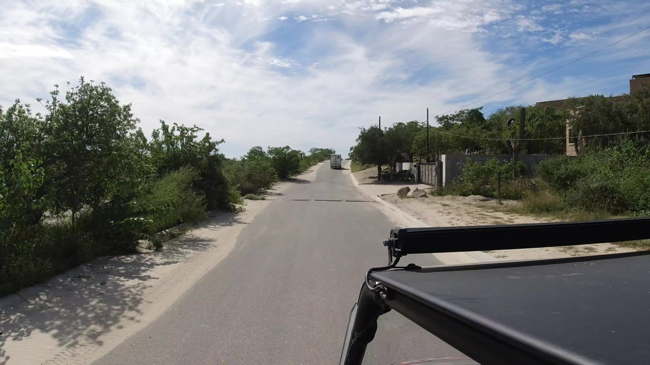 Paved road viewed over a black vehicle rack with shrubs on both sides.