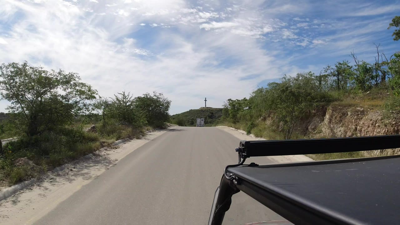 Narrow paved road with shrubs and low hills ahead under a bright sky.