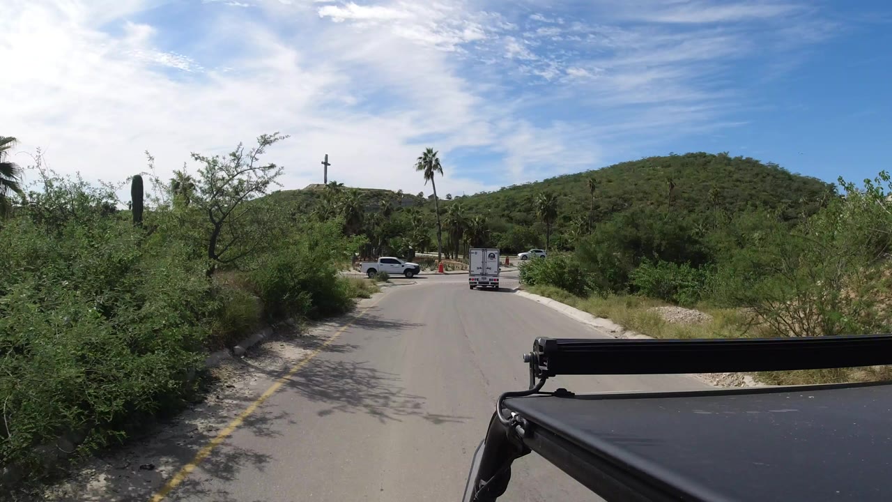 Vehicle-mounted view down a paved road toward a white truck and green hills.