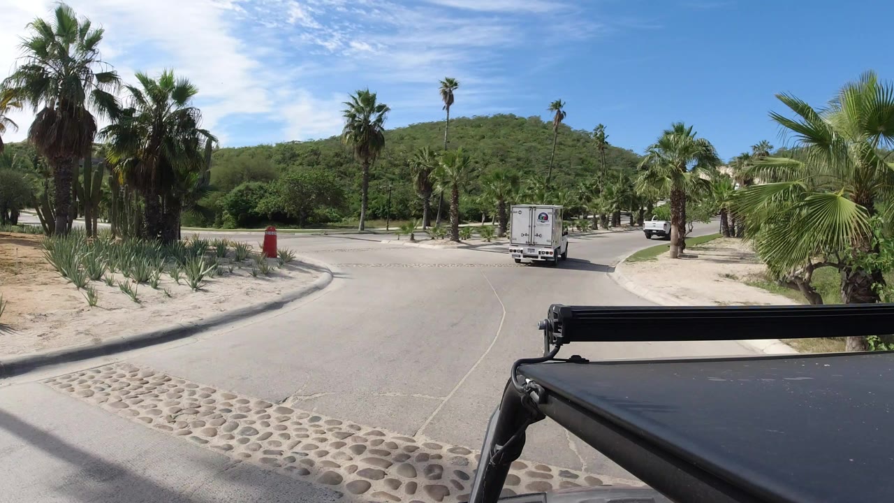 At the start of the Los Cabos, Mexico clip, a white delivery truck drives ahead on a paved road bordered by palms and desert landscaping, with no visible people.