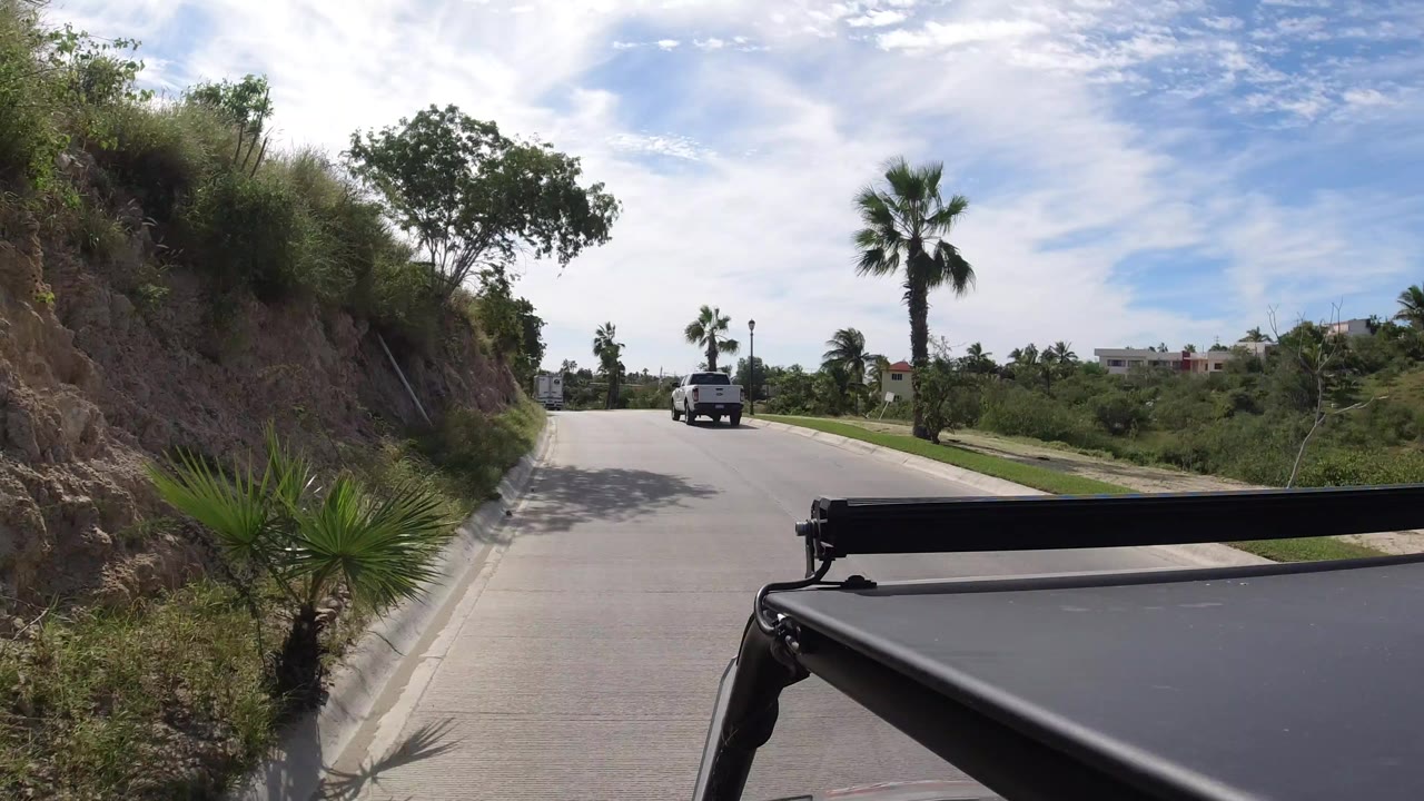 Vehicle-mounted view down a paved road with palms and a truck ahead.