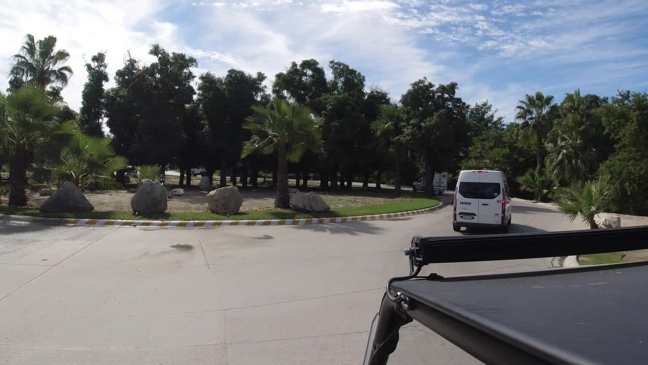 White van ahead on a sunny landscaped road with palms and rocks.