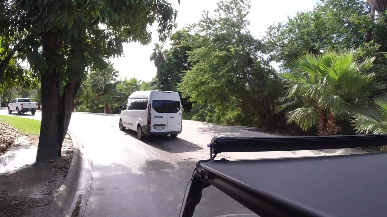 White van on a curved sunlit street with palms and trees.