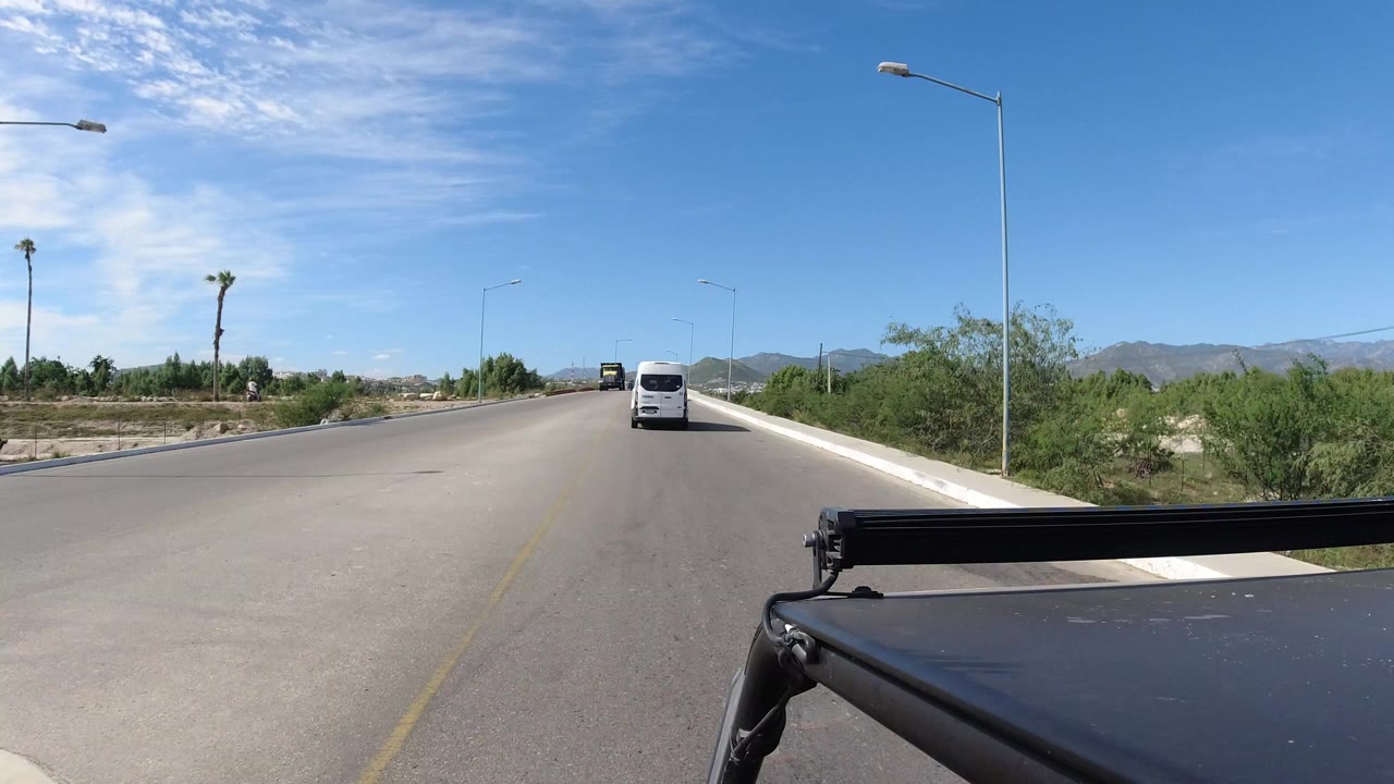Sunny road with a white van ahead and green roadside trees.