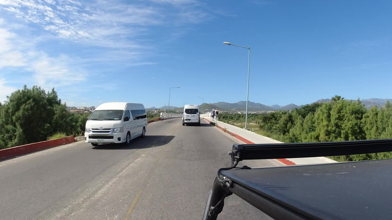 White vans on a paved road with greenery and mountains
