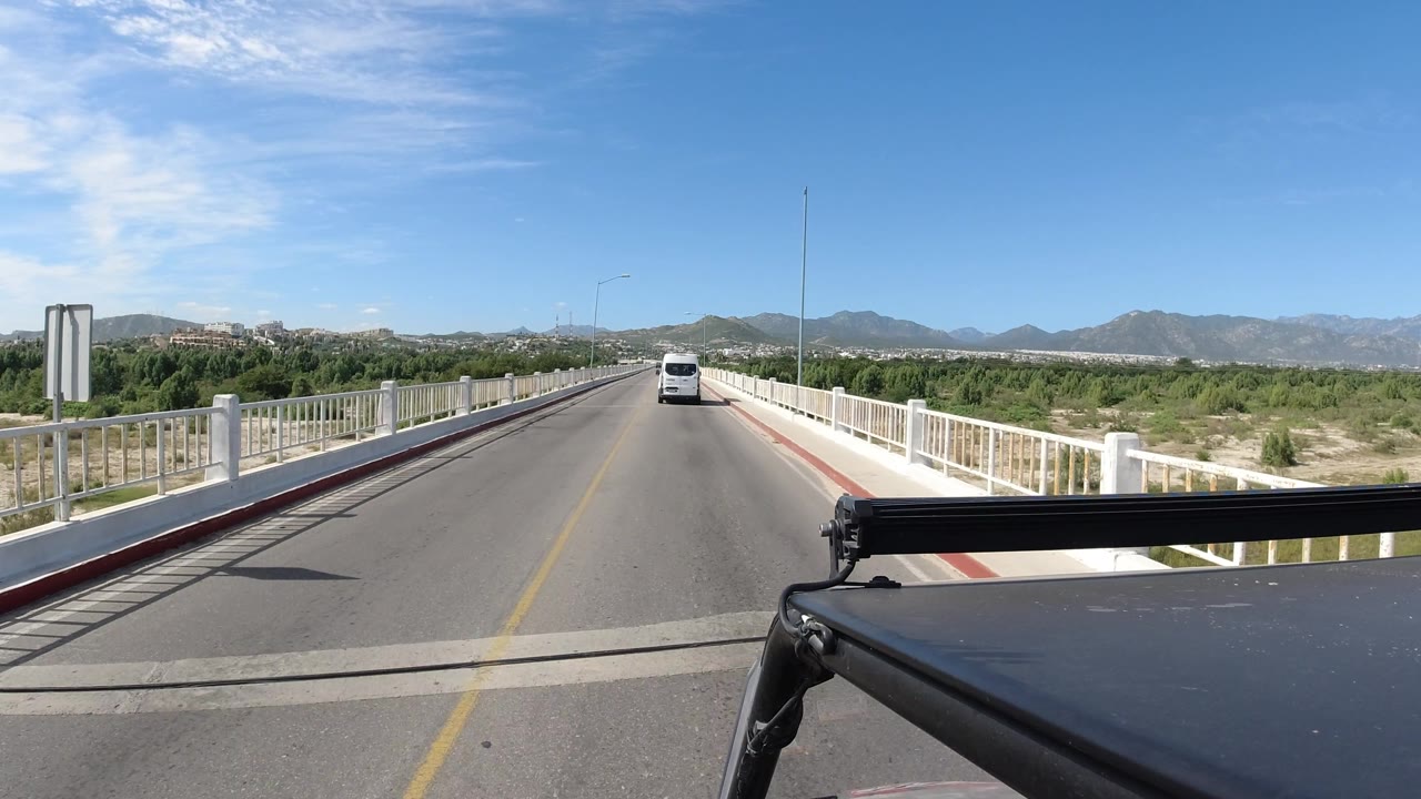 Straight bridge road with a white van ahead under a clear blue sky.