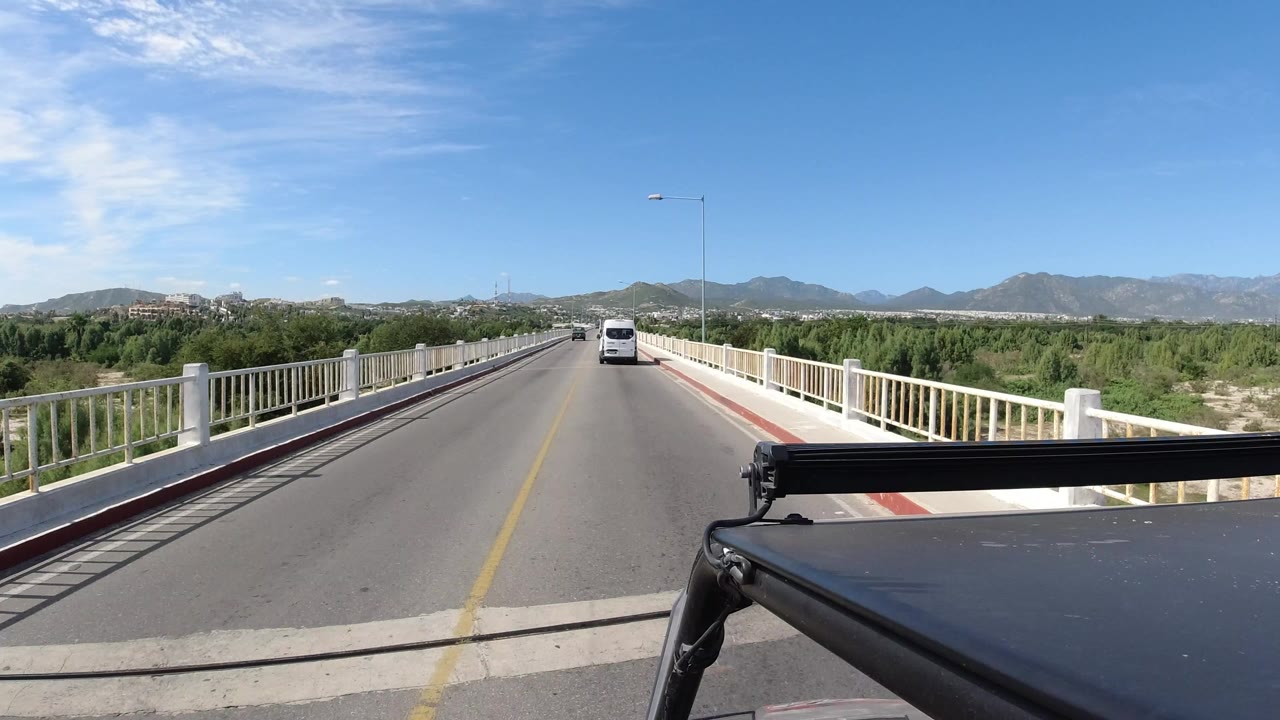 Forward view from a vehicle on a bridge road with a white car ahead.