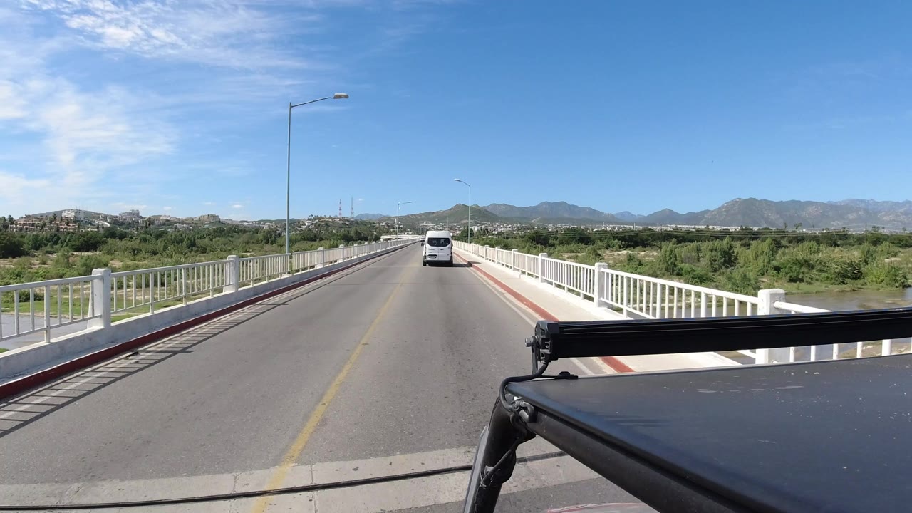 Forward view from a black vehicle crossing a bridge behind a white van.