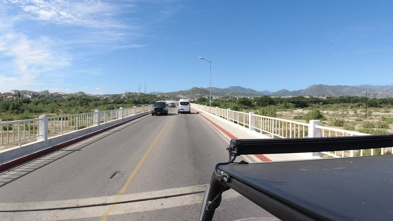 A white van and a dark car drive ahead on a bridge road.