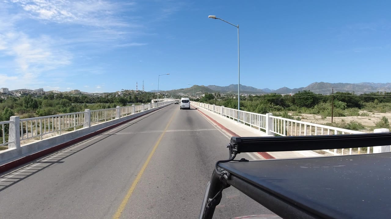 Straight bridge roadway under blue sky with a car in the distance.