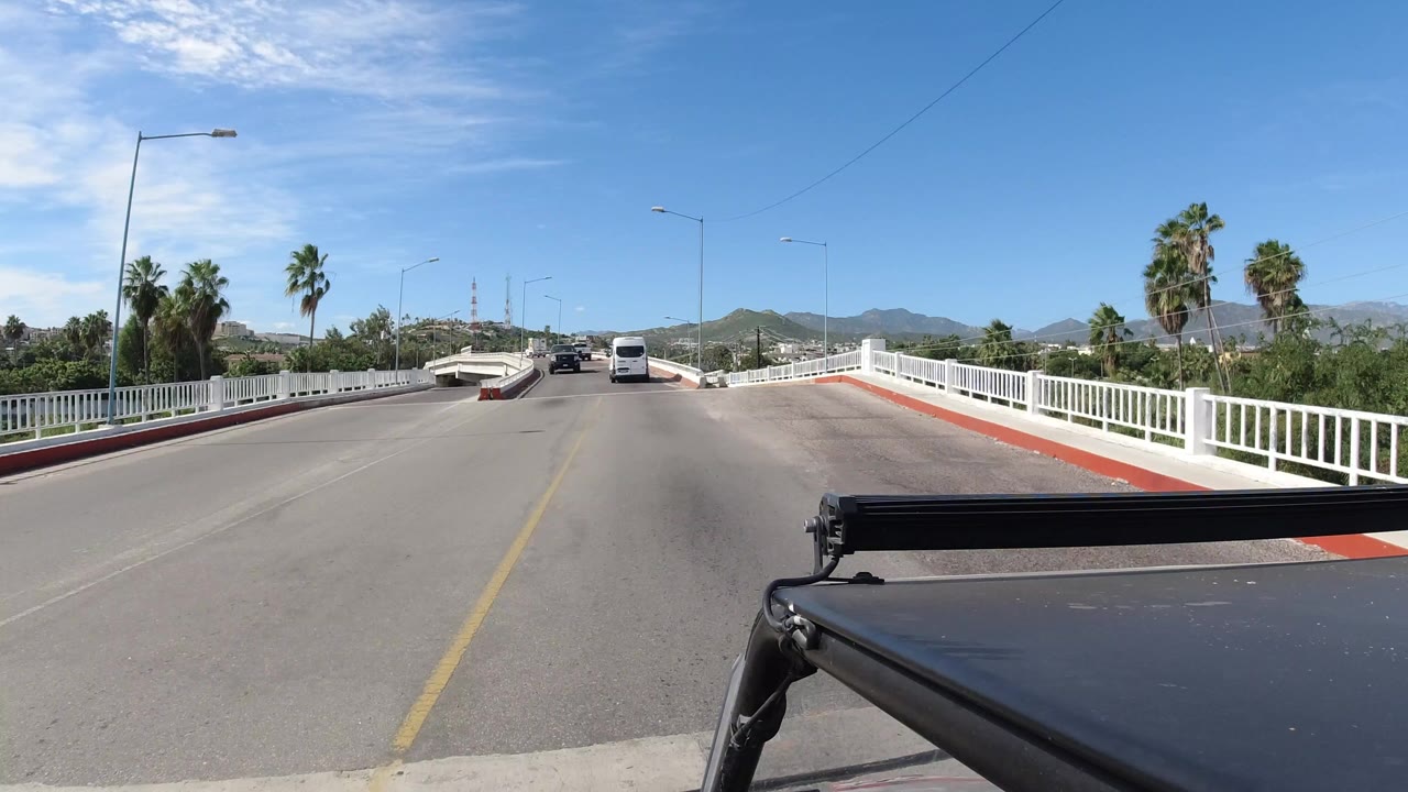 Forward road view on a bridge with white railings and hills ahead.