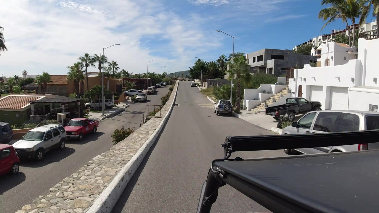 Uphill residential street with parked cars and white homes