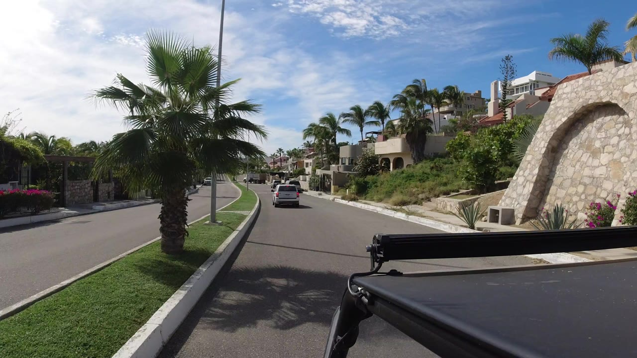 Residential road with cars, palms, stone arch, and dark foreground rail