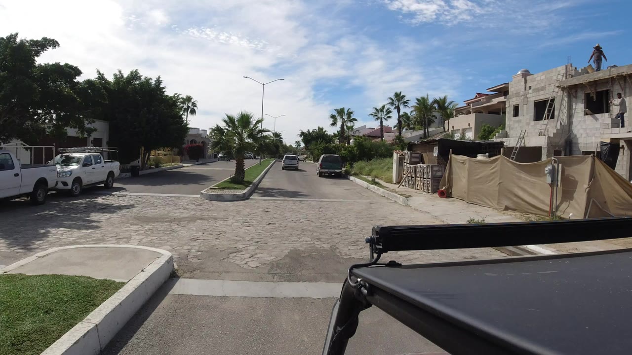Residential road with palms, construction site, and vehicles