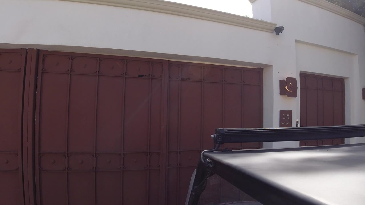 Parked car roof in front of a red garage gate and white wall.