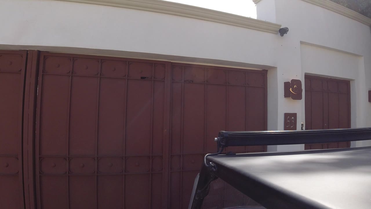 Red wooden doors on a white stucco building behind a vehicle roof rail.