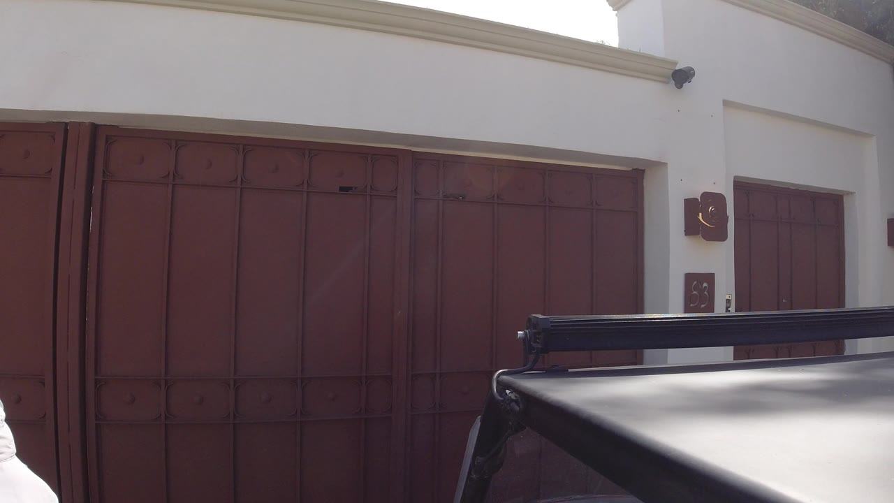 Reddish iron gates and a dark vehicle roof under a white stucco porch.