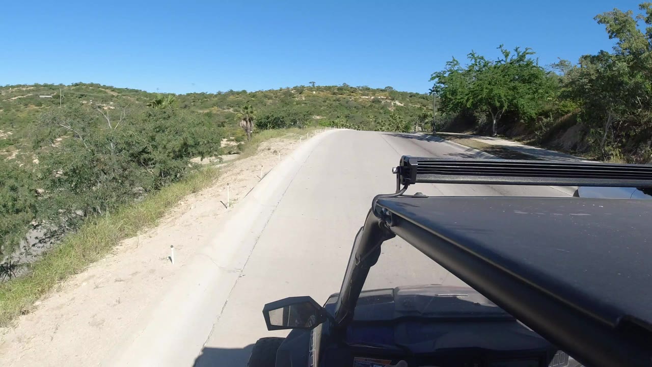 Paved road ahead with vehicle roof rack and dry green hillsides.
