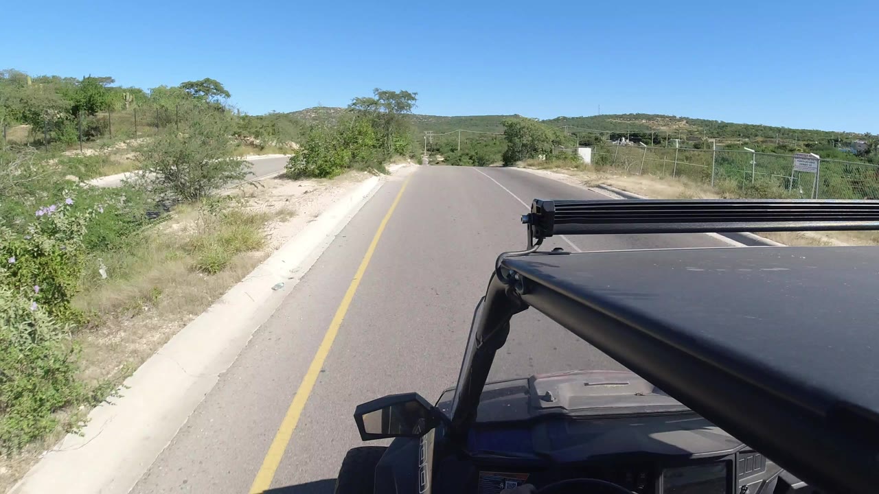 Jeep roof foreground on a sunny rural road bordered by brush.