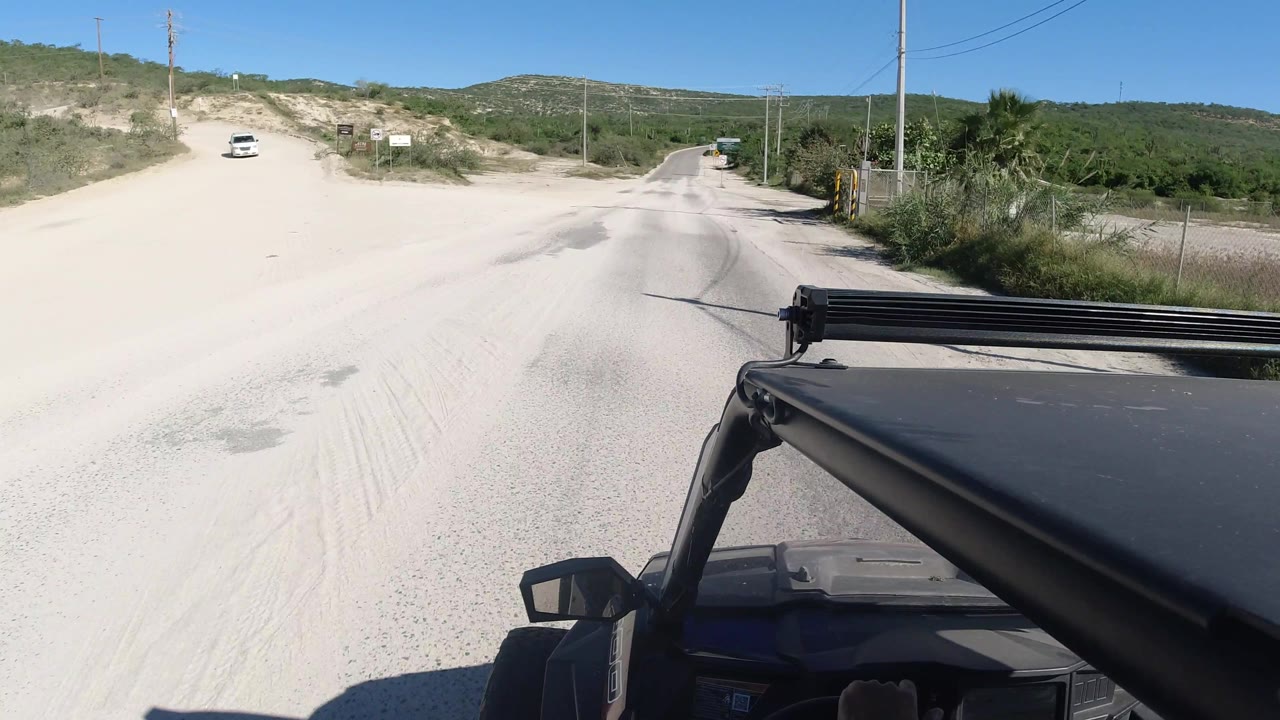 Dusty road ahead with Jeep hood, poles, signs, and hills