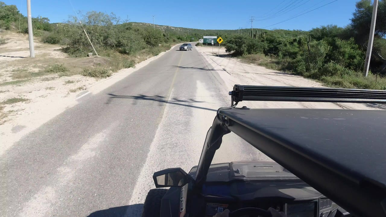 Paved road ahead with vehicle roof in foreground and desert scrub on both sides.