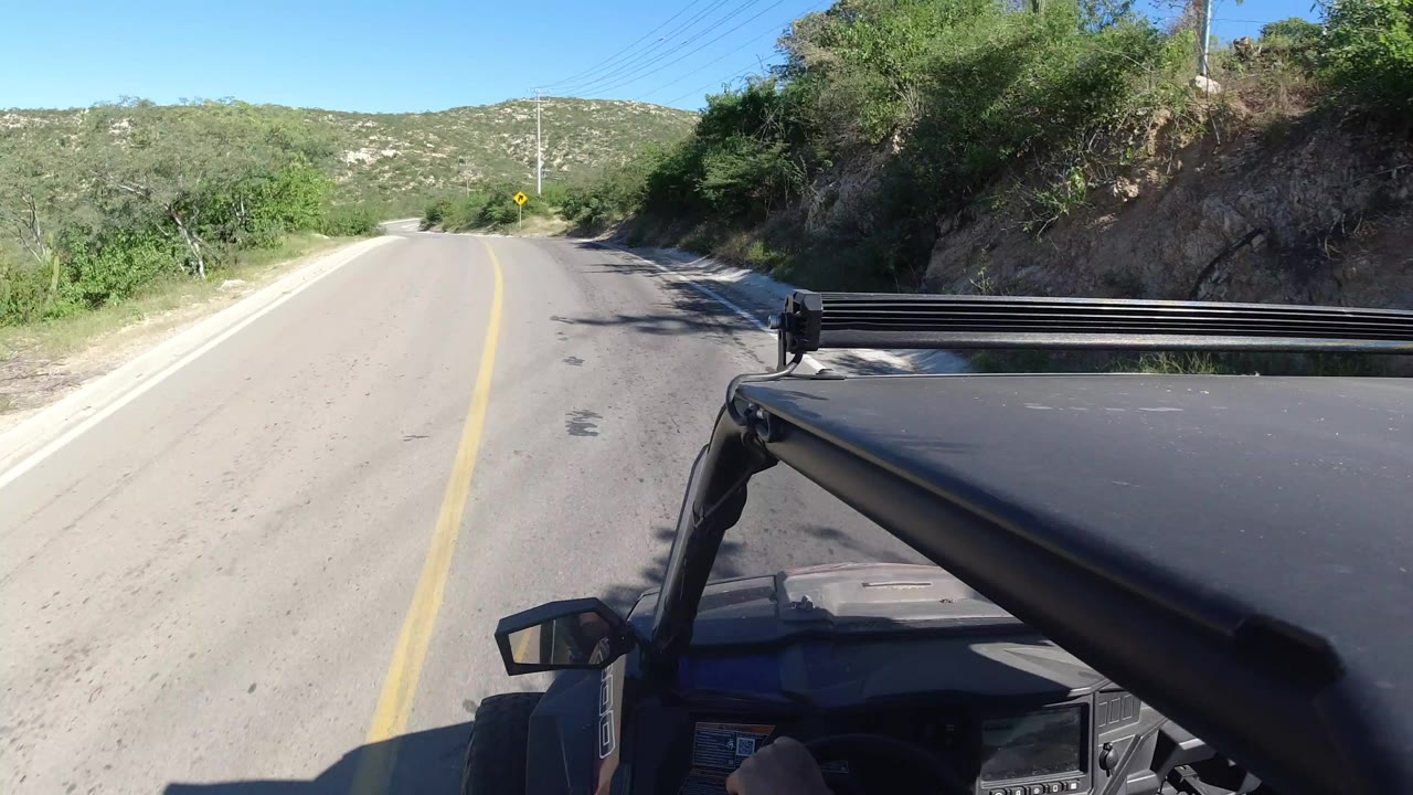 Vehicle-mounted view of a quiet paved road through green hills.