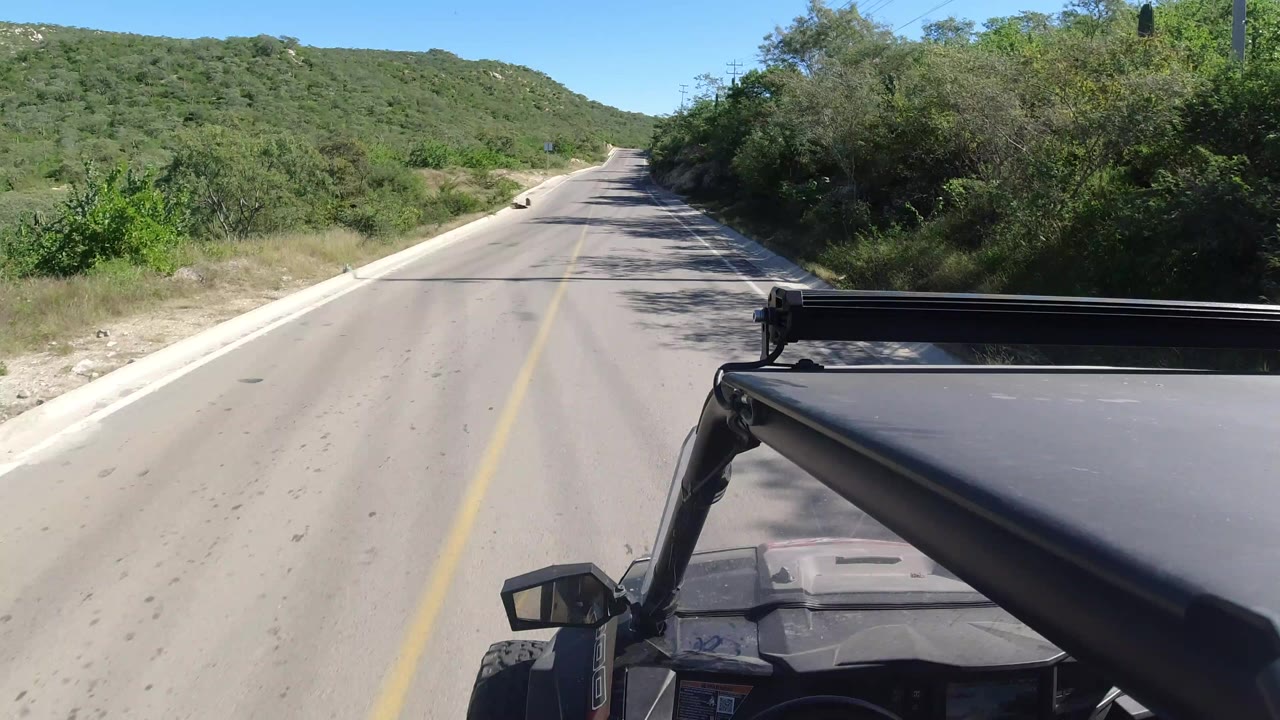 Empty paved road through green hills seen from a moving vehicle.