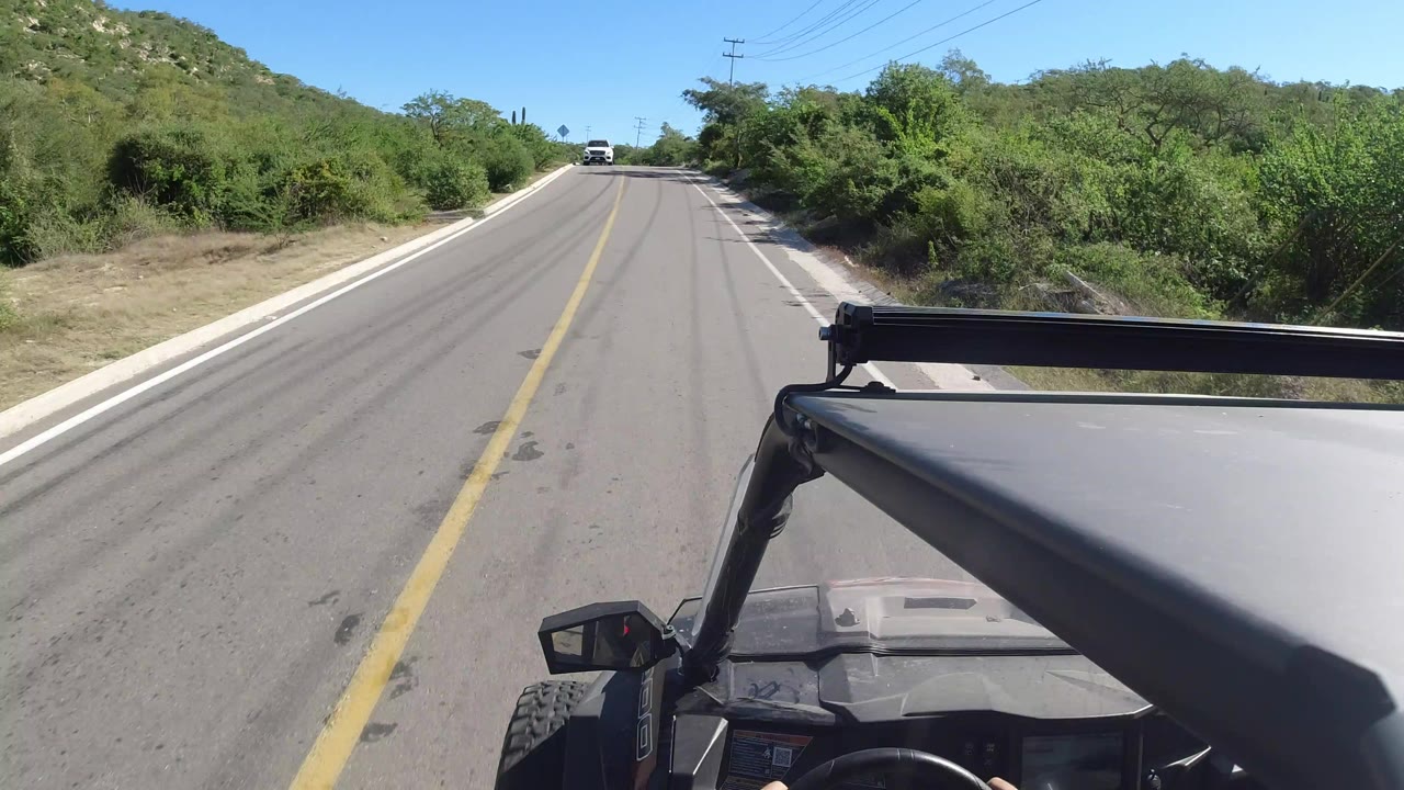 Two-lane road through green hills seen from an open vehicle.