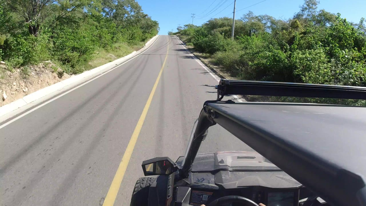 Open vehicle driving on a two-lane road bordered by green bushes.