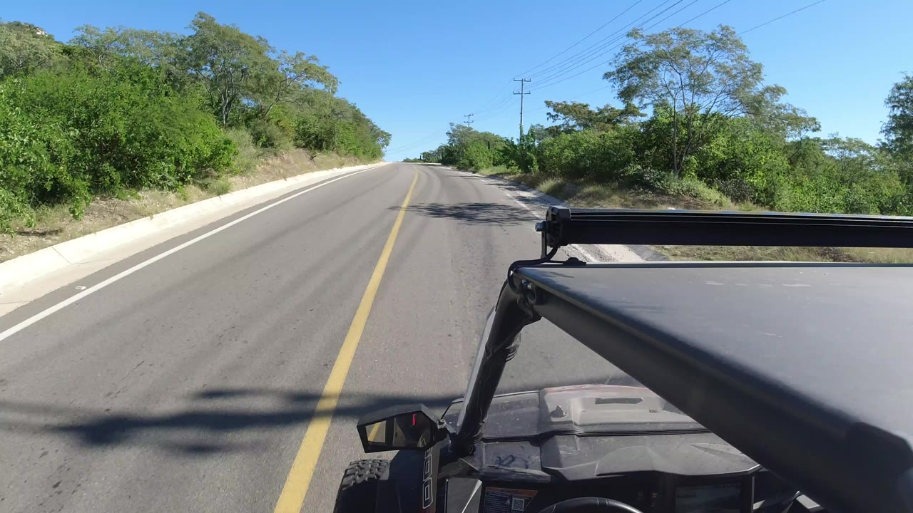 Paved road ahead with vehicle roof in foreground and green brush on both sides.