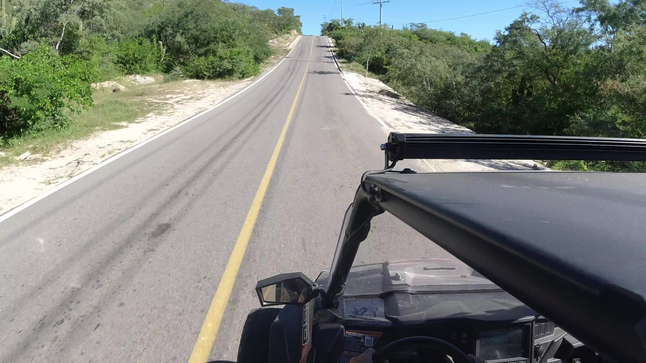 Empty paved road with scrub vegetation and vehicle hardware