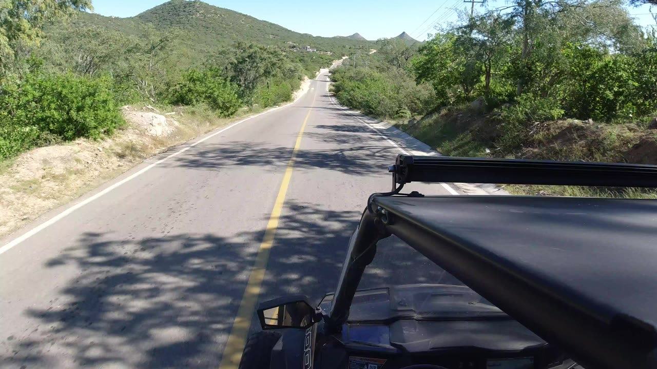 Two-lane road ahead with vehicle roof in foreground and green hills beyond.