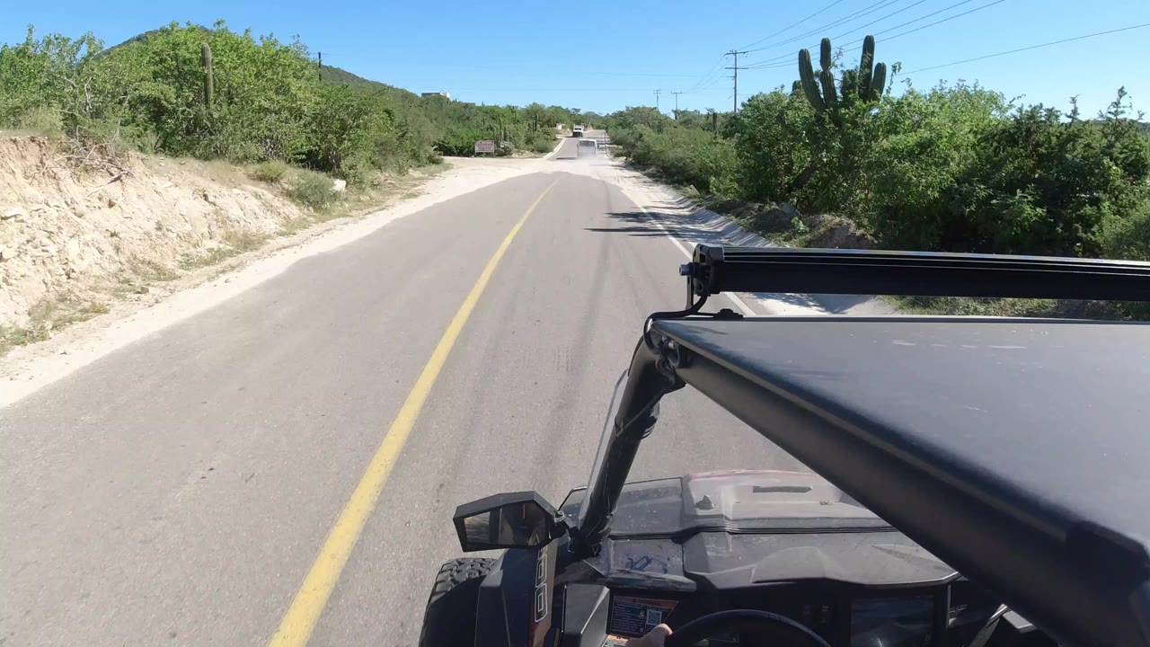 Paved road through green vegetation with vehicle roof in the foreground.