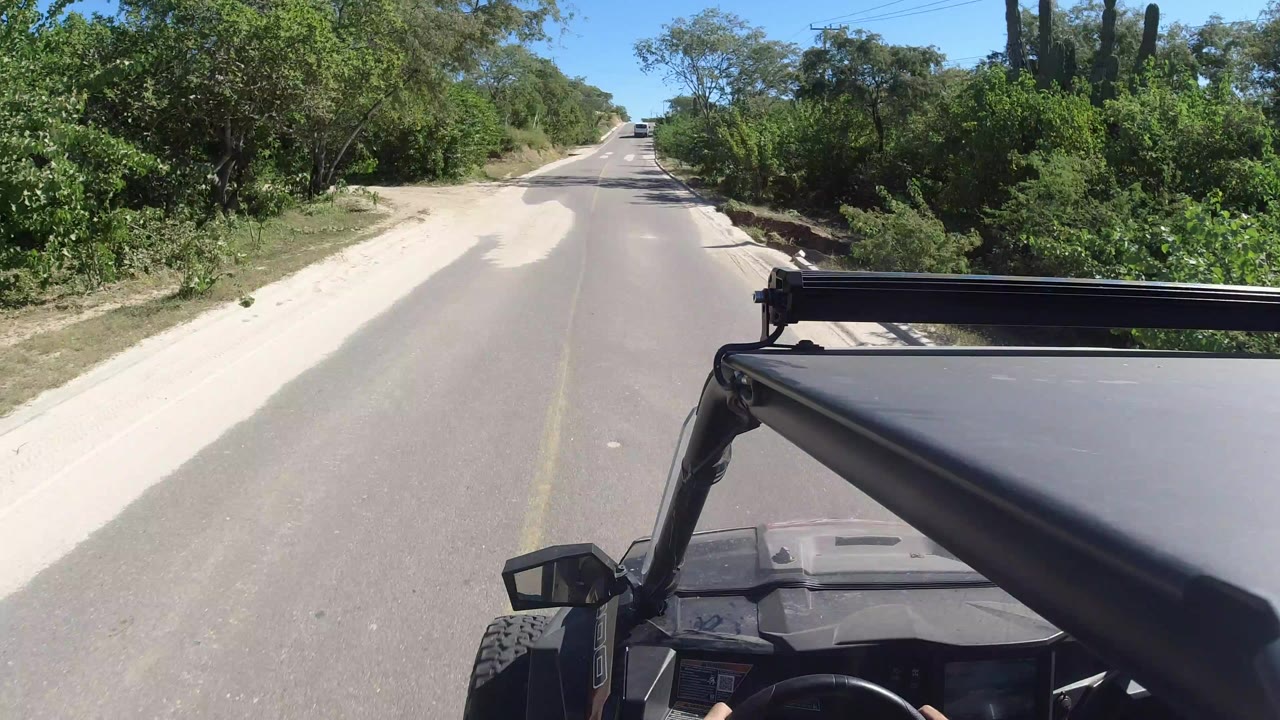 Jeep roof and windshield edge on a sunlit two-lane desert road