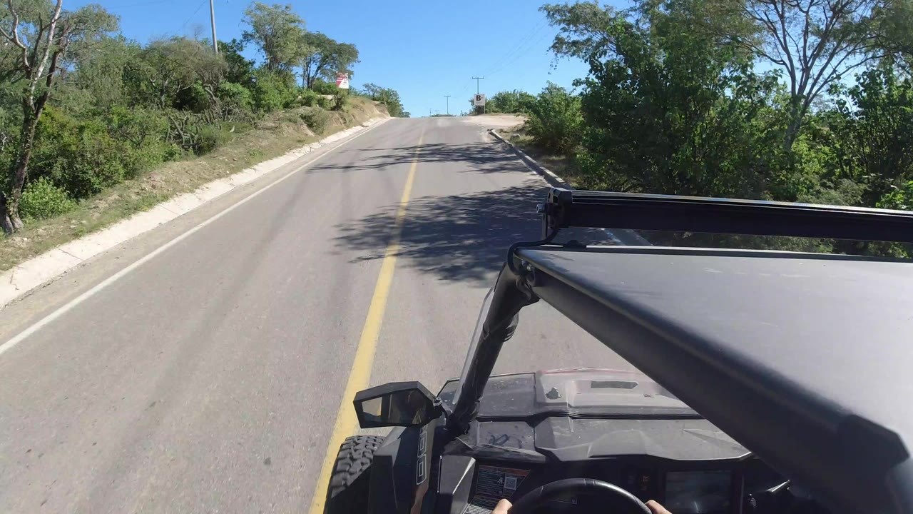Jeep roof and roll bar facing up a sunny paved road.