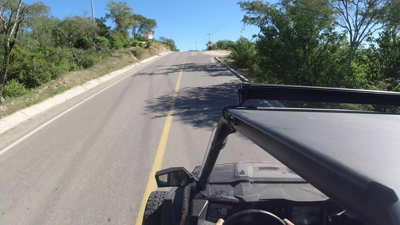 The camera remains over the jeep as the road rises slightly through green vegetation in Los Cabos, Mexico, with no visible people in frame.
