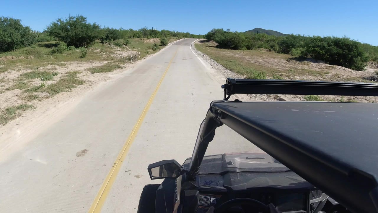 Paved road ahead with vehicle roof and roll bar in foreground