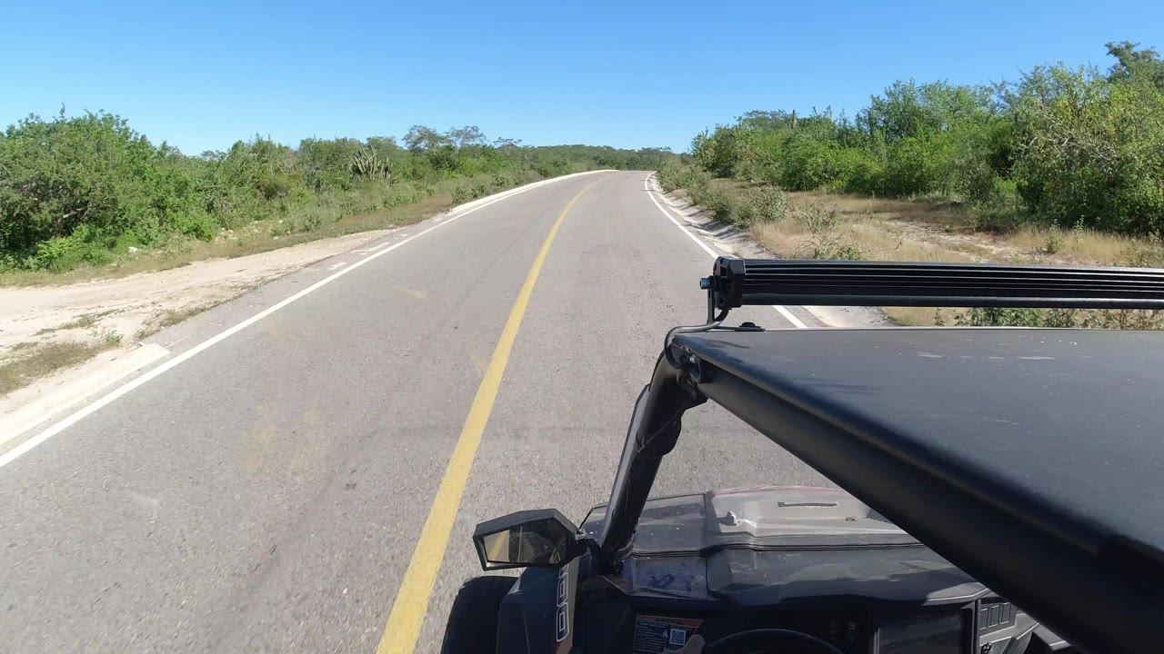 Forward view down a sunny two-lane road with vehicle roof visible