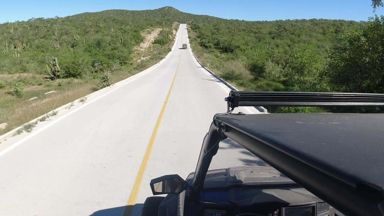 Vehicle-mounted view of a quiet highway bordered by dense green brush.