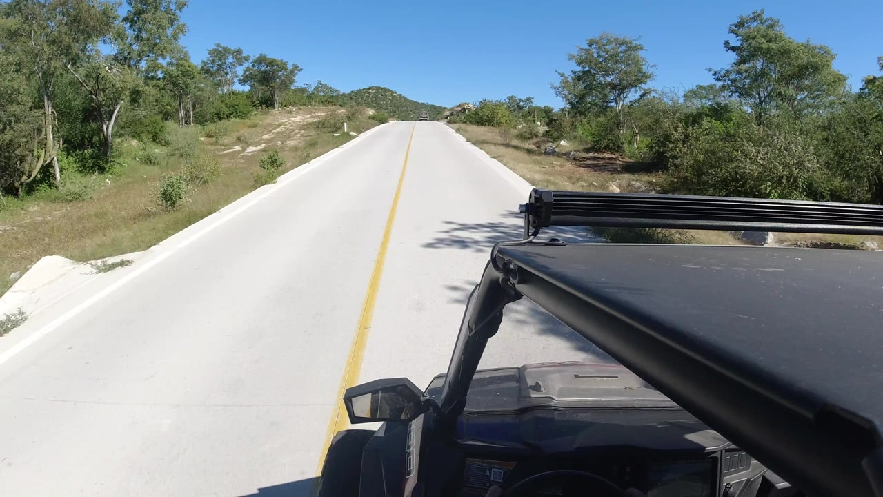 Bright road view with roadside vegetation and vehicle hardware at right.