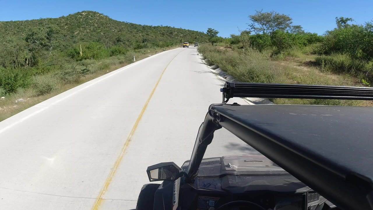 Open road through green hills from a vehicle-mounted view.