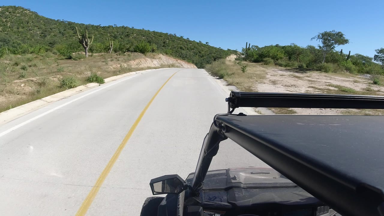 Two-lane road curving through dry roadside cuts with desert vegetation on both sides.