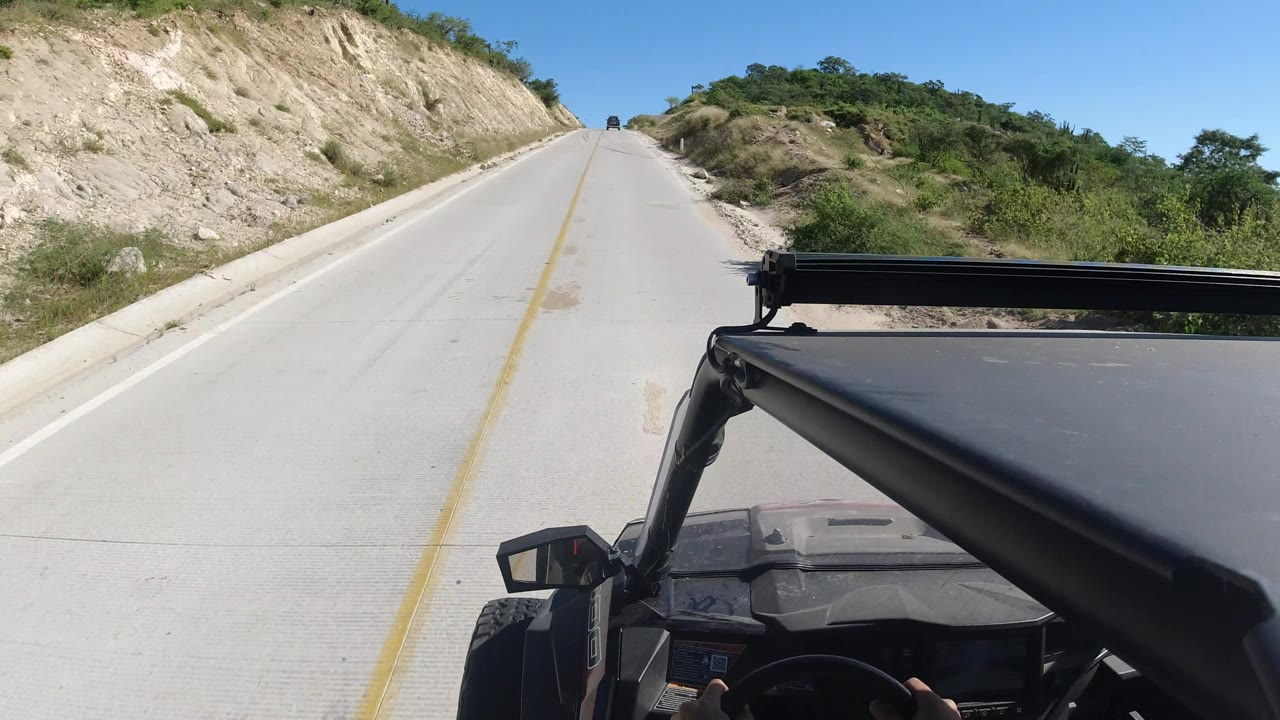 Open highway passing low hills and shrubs under clear daylight.