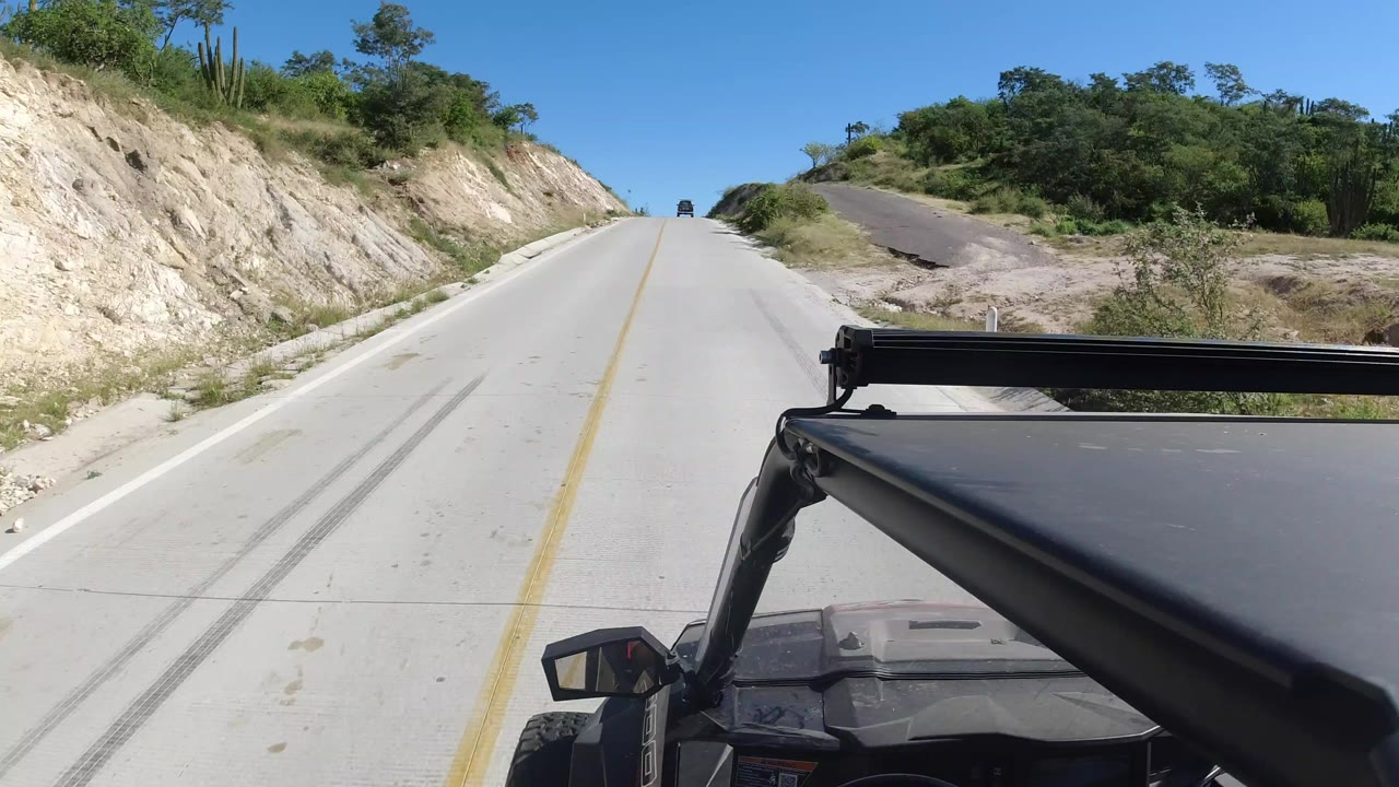 Vehicle-mounted view up a pale highway between sandy banks.