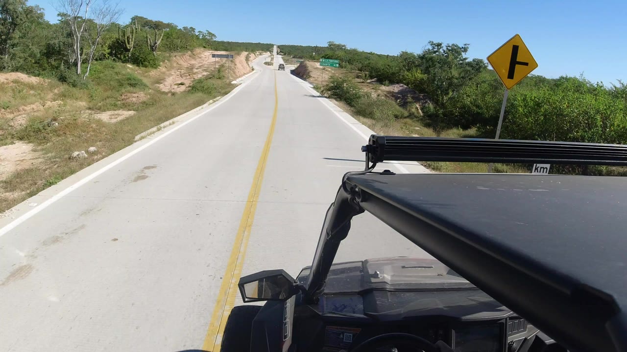 Forward view from a Land Rover on a pale road with a yellow turn sign