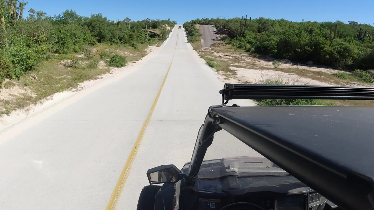 Straight pale road through brush with the black SUV foreground on the right.