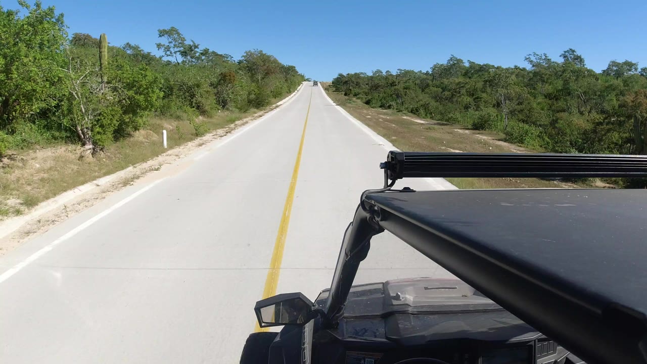 Jeep foreground on a straight concrete road through green countryside.